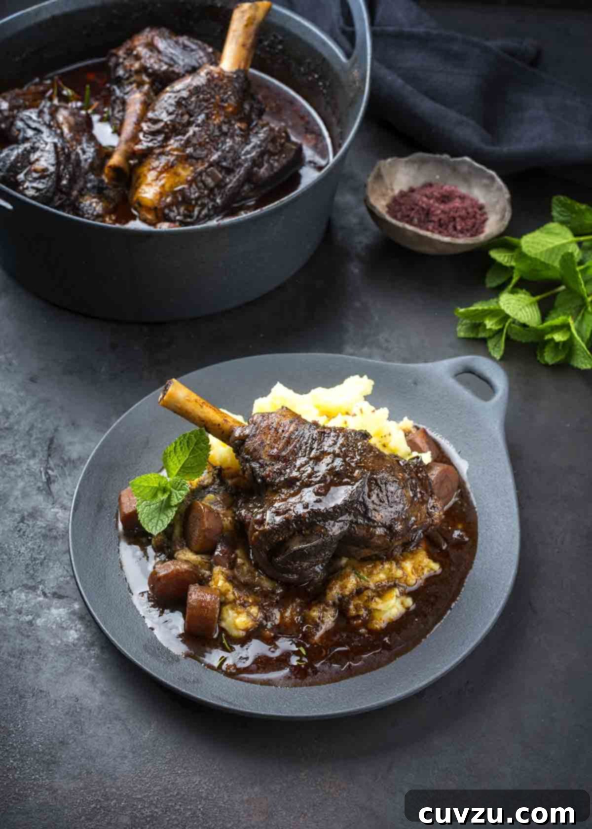 Braising Explained 2 A grey plate topped with braised lamb, mashed potatoes, carrots, and gravy as an illustration of what is braising, emphasizing comfort and rich flavor.