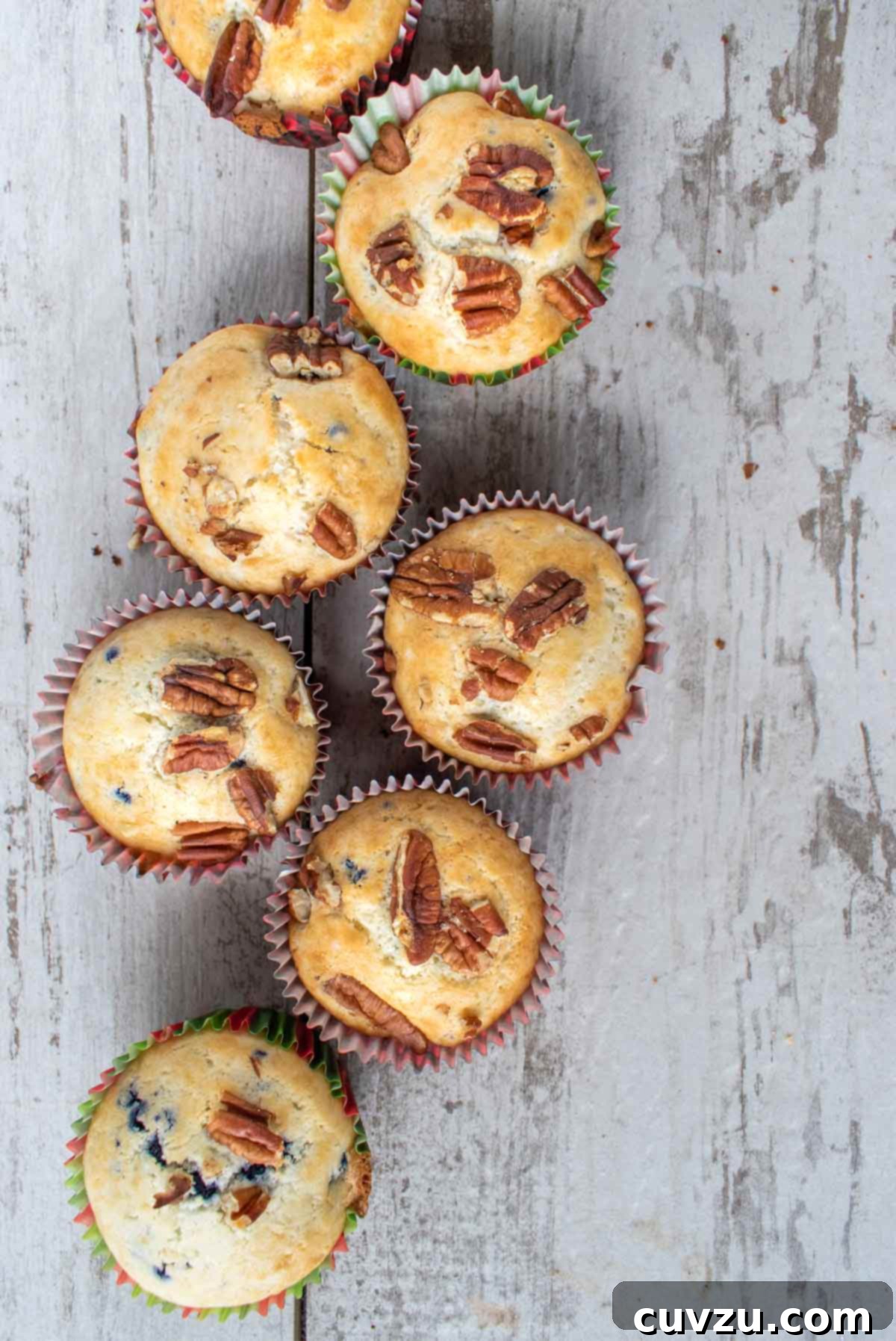 Five beautifully baked blueberry pecan muffins with a crumb topping, arranged on a rustic wooden surface.