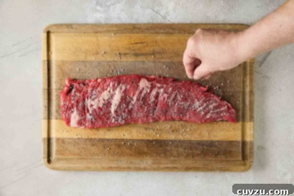 Flame-Kissed Skirt Steak with Vibrant Salsa 12 A person seasoning a skirt steak on a cutting board with salt.