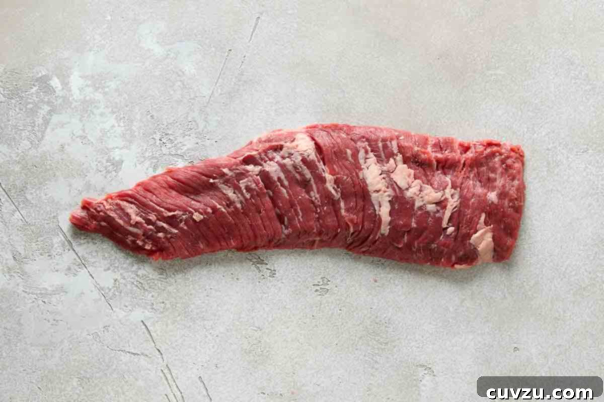 An uncooked, raw piece of skirt steak, showing its characteristic long, thin shape and distinct grain.