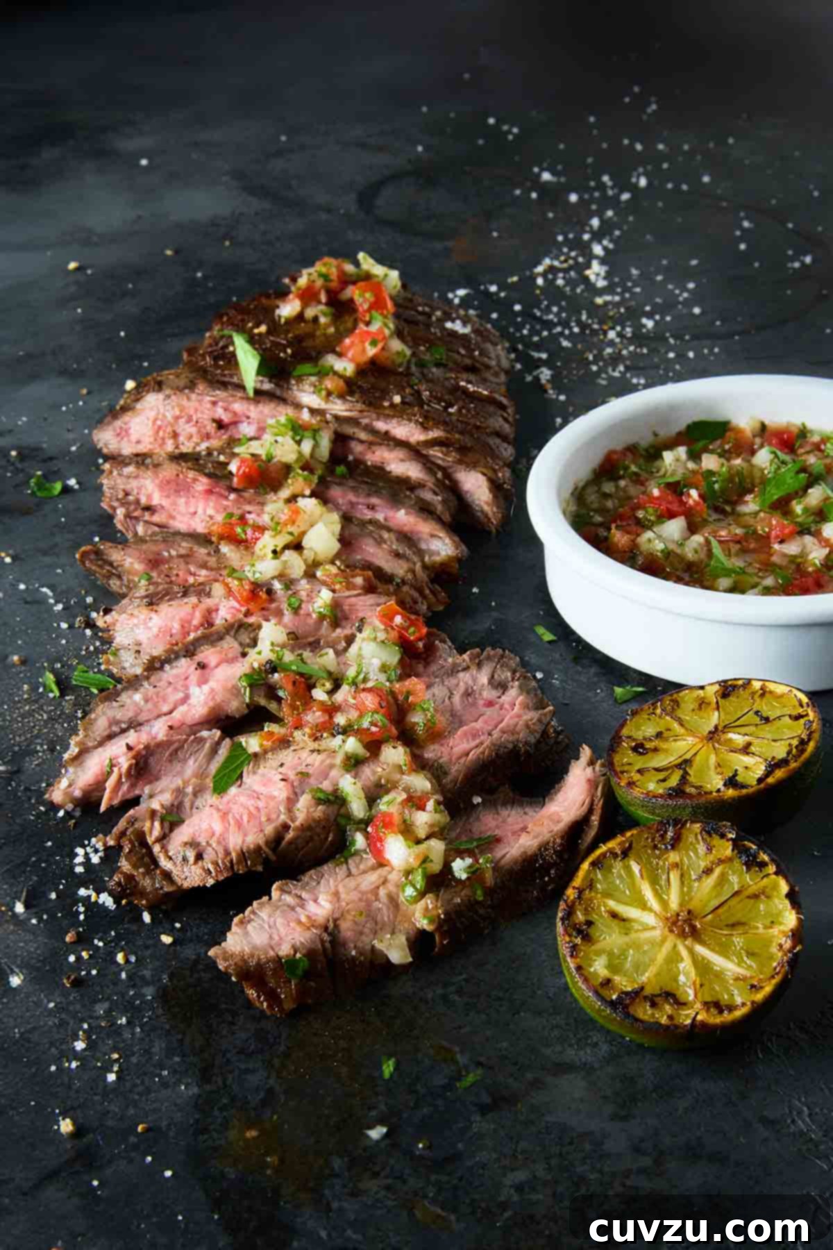 Flame-Kissed Skirt Steak with Vibrant Salsa 9 A beautifully presented dish of sliced seared skirt steak generously topped with homemade salsa. A small bowl of extra salsa and charred lime halves are placed alongside, inviting enjoyment.
