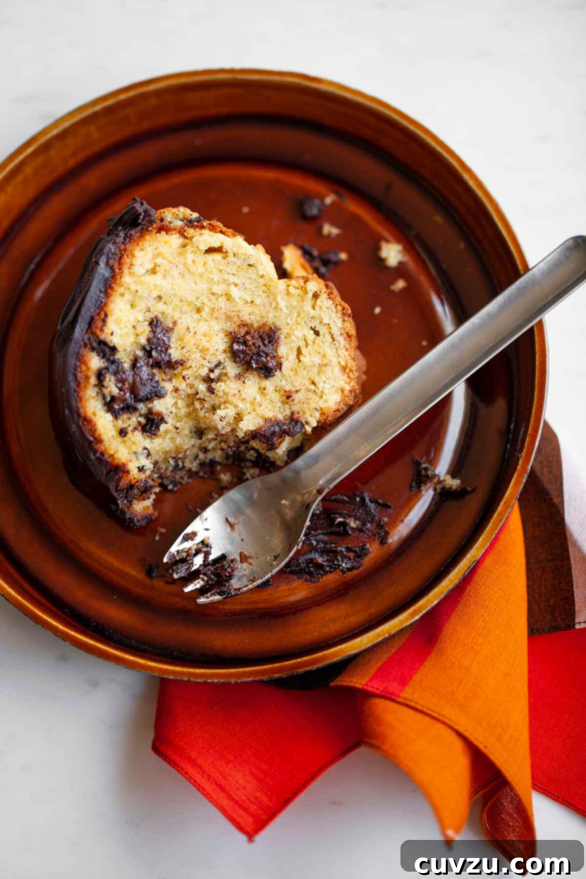 Zesty Orange Chocolate Chunk Indulgence 3 A perfectly sliced orange chocolate chunk cake on a brown plate, accompanied by a fork and an orange napkin.