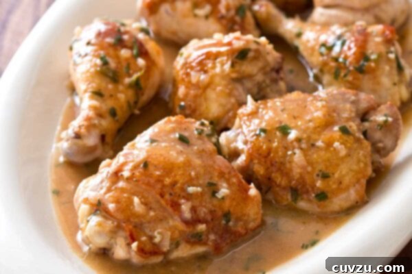 Pieces of pan roasted tarragon chicken arranged in a white serving platter with a glass measuring cup and spoon in the background.