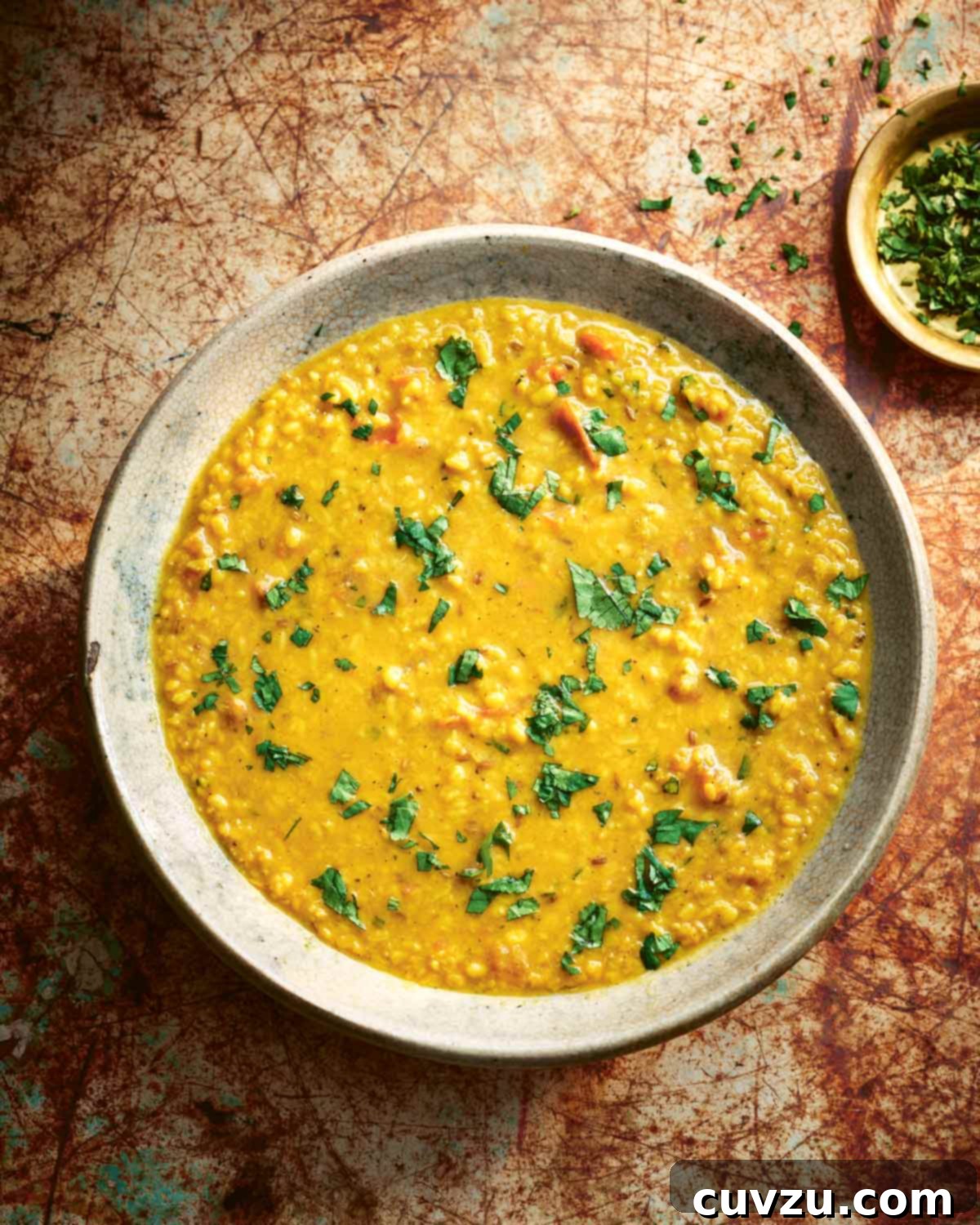 Aromatic Tarka Dal with Tomato and Cilantro 2 A ceramic bowl filled with tarka dal and sprinkled with cilantro with a small bowl of chopped cilantro on the side.