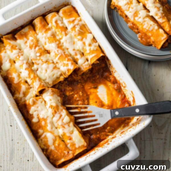 No-Fuss Flavorful Chicken Enchiladas 3 A rectangular dish of easy chicken enchiladas with a spatula resting in the dish and a couple enchiladas on a grey plate beside it.
