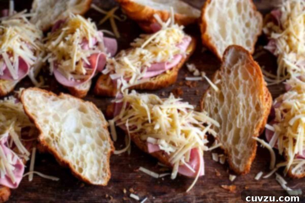 Open croissants generously filled with slices of savory ham and a liberal sprinkle of shredded cheese, ready to be quartered and assembled for the casserole.