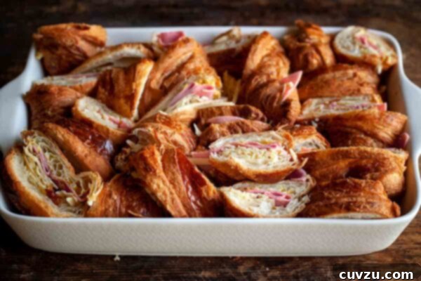 An assembled Croque Monsieur casserole, pre-baked, with croissant pieces nestled together in the dish, revealing layers of ham and cheese.