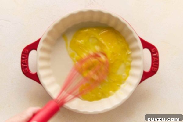 Golden Skillet Chicken Bites 13 A person's hand whisking egg in a pie plate.