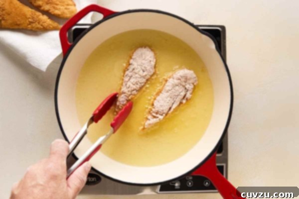 Golden Skillet Chicken Bites 17 A person frying chicken tenders in a skillet.