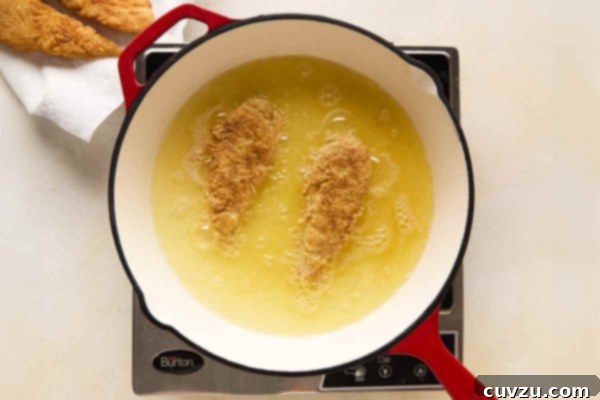 Golden Skillet Chicken Bites 18 A person frying chicken tenders in a skillet.