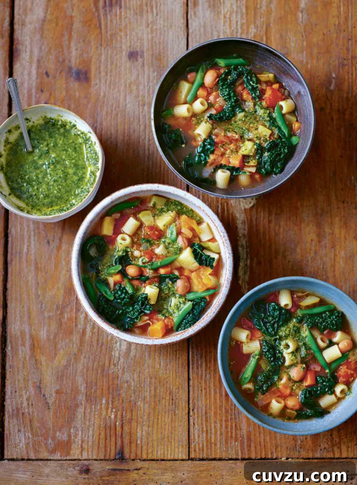Three rustic bowls of vibrant old-fashioned minestrone soup, with a small bowl of fresh green pesto on the side.