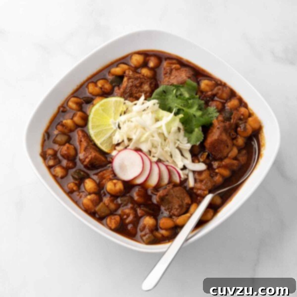 Hearty Instant Pot Pork Pozole 3 A square white bowl filled with Instant Pot pork pozole, garnished with radish, shredded cheese, lime, and cilantro, with a spoon resting in it.