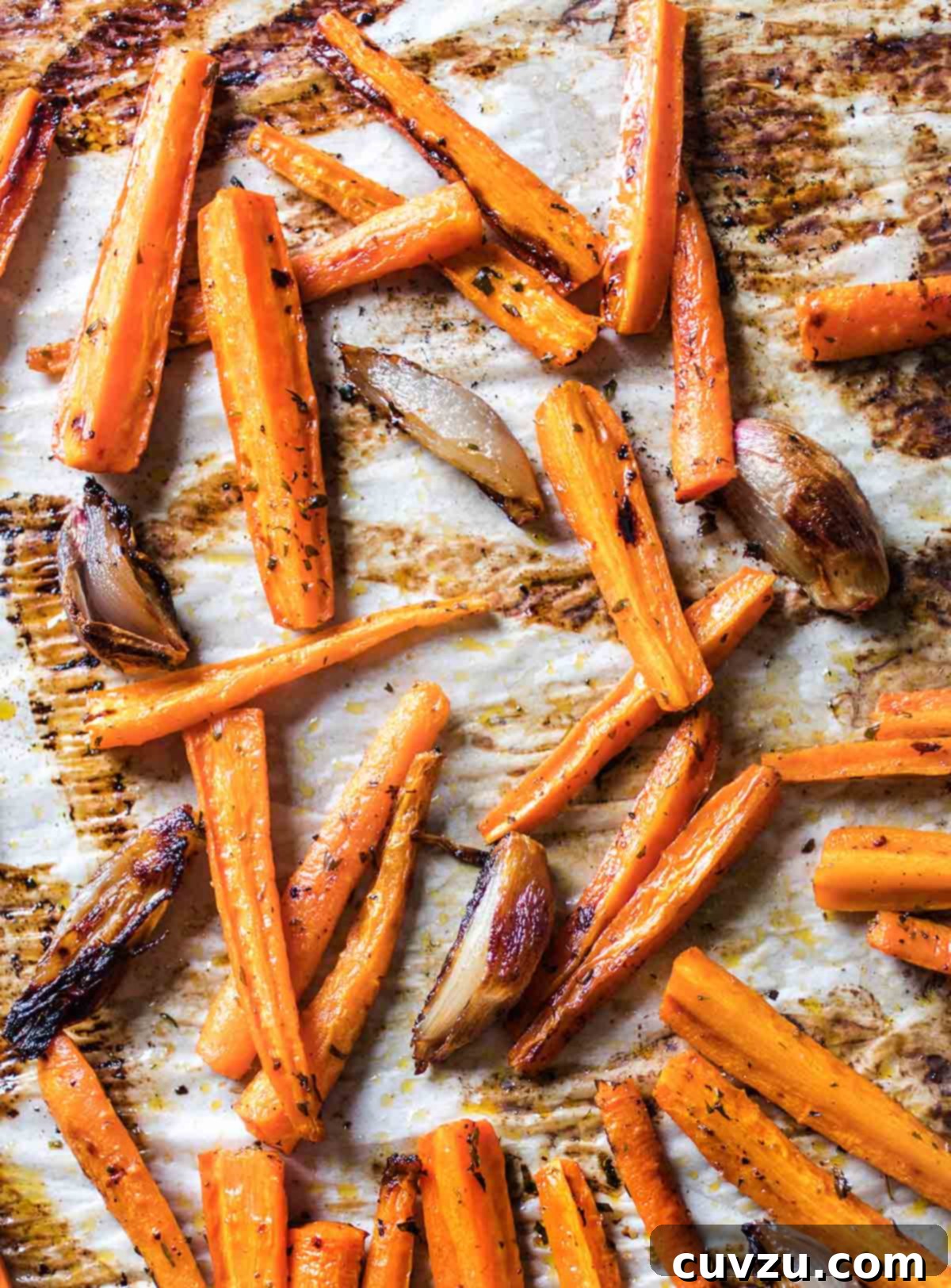 A baking sheet lined with parchment and covered with easy roasted carrots and onions with burnt edges.