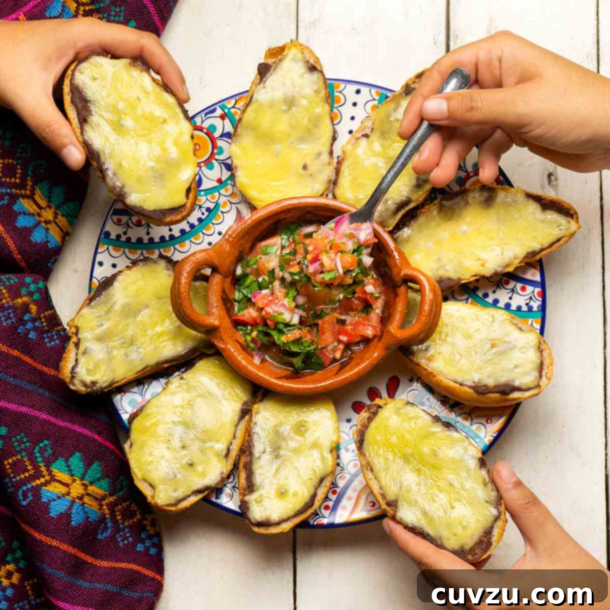 Two people reaching for traditional molletes on a platter with a bowl of salsa in the middle.