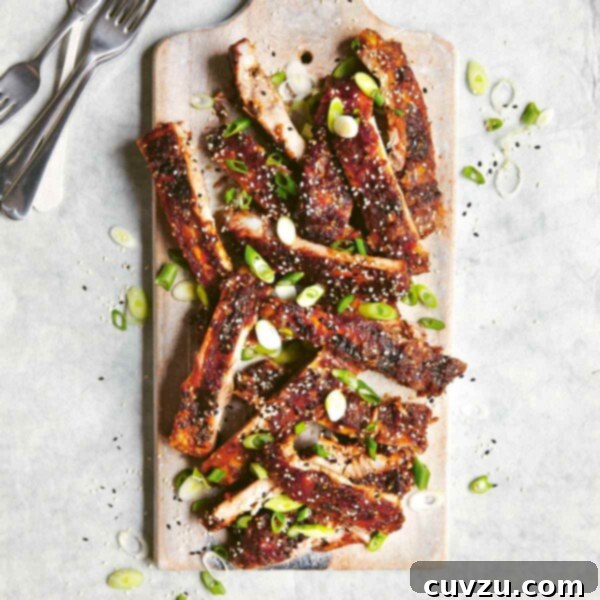 A pile of Korean-style BBQ ribs on a wooden board, garnished with scallions and sesame seeds with several forks on the side.