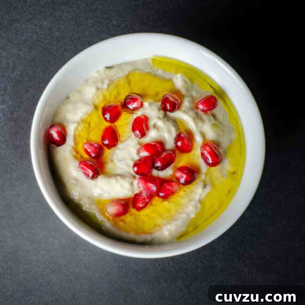 Moutabal Smoky Roasted Eggplant Yogurt Tahini Dip 5 A bowl of creamy Moutabal dip, artfully garnished with a swirl of olive oil and a sprinkle of ruby-red pomegranate seeds, ready for serving.