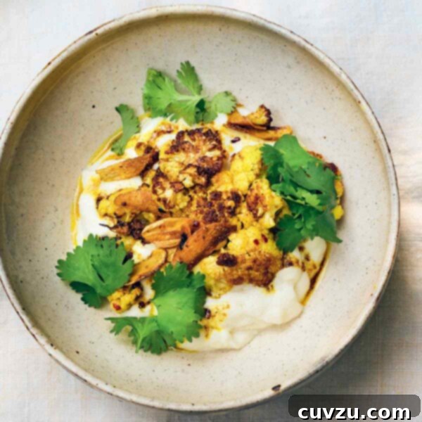 A ceramic shallow bowl filled with cauliflower puree with garlic and spices and roasted cauliflower and cilantro on top.