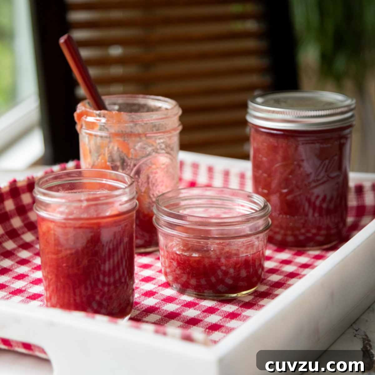 Rhubarb Savvy: Pick It, Keep It, Freeze It 11 Four jars of rhubarb jam on a white tray lined with checkered cloth, showcasing a homemade feel.