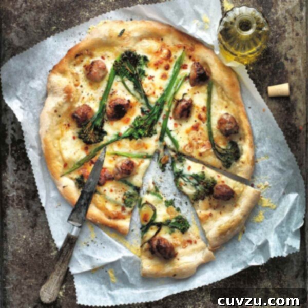 A white pizza with broccolini, fontina, and sausage cut into slices on a piece of parchment with a knife on top and a bottle of oil on the side.