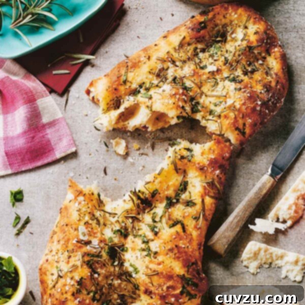 A torn loaf of focaccia with herbs and salt and sprigs of rosemary, a knife, and a hunk of pecorino on the side, showcasing its irresistible texture and rich color.