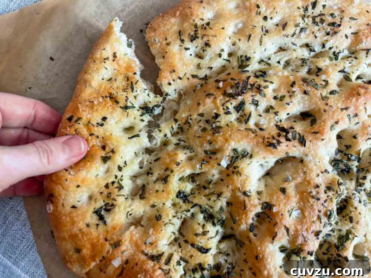 Focaccia 6 A beautifully torn loaf of cheesy focaccia, garnished with rosemary and sea salt, beside a knife and a wedge of Pecorino cheese.