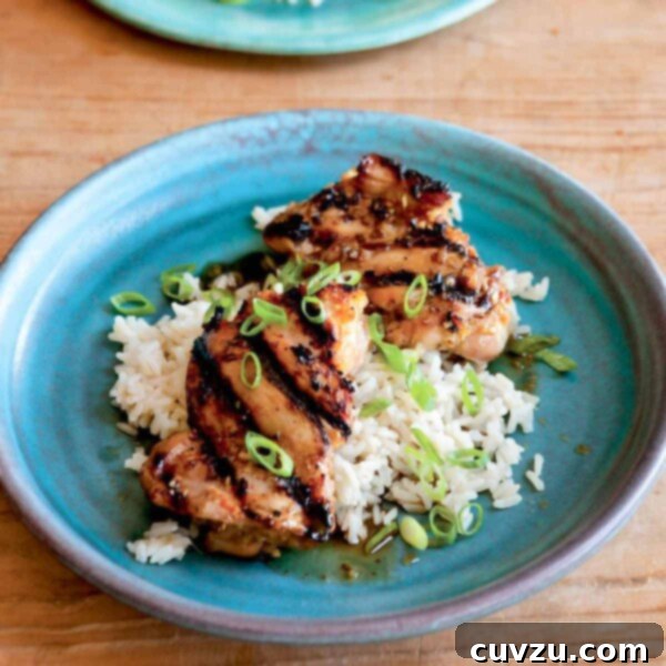 Two pieces of grilled lemongrass chicken on top of rice with scallion garnish on a blue plate.