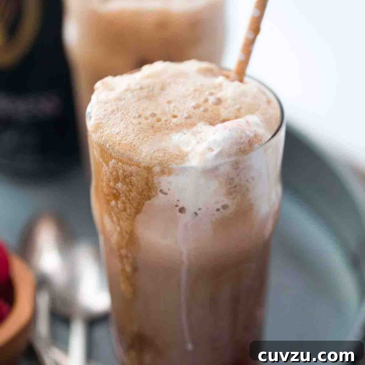 Two Guiness floats with straws on a grey metal try with a few spoons lying beside them.