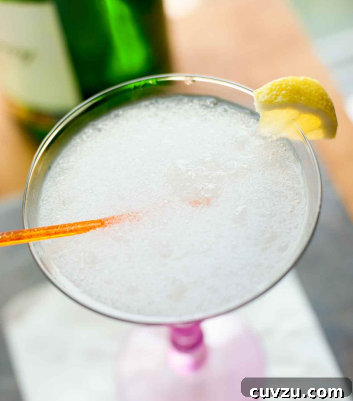 A frozen gin fizz in a martini glass with an orange stir stick and a little piece of lemon on the rim.