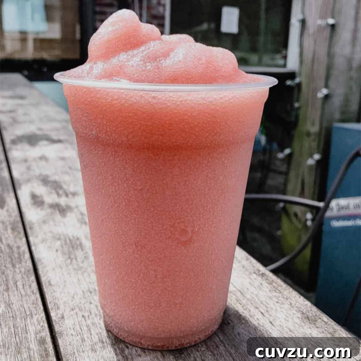 A tall plastic cup filled with frosé or frozen rosé on a wooden table.