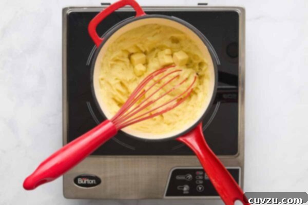 A pot filled with mashed potatoes with cubes of butter on top and a whisk resting inside.