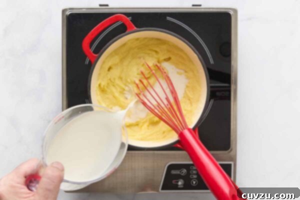 A person adding milk to a saucepan of mashed potatoes.