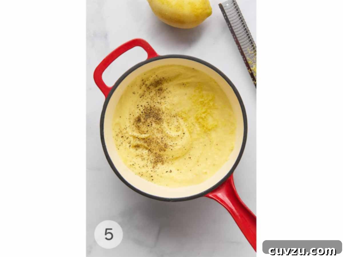 Ina Gartens Bright Lemony Mashed Potatoes 8 A close-up view of a saucepan filled with perfectly mashed potatoes, now delicately seasoned with bright lemon zest and a generous sprinkle of freshly ground black pepper.