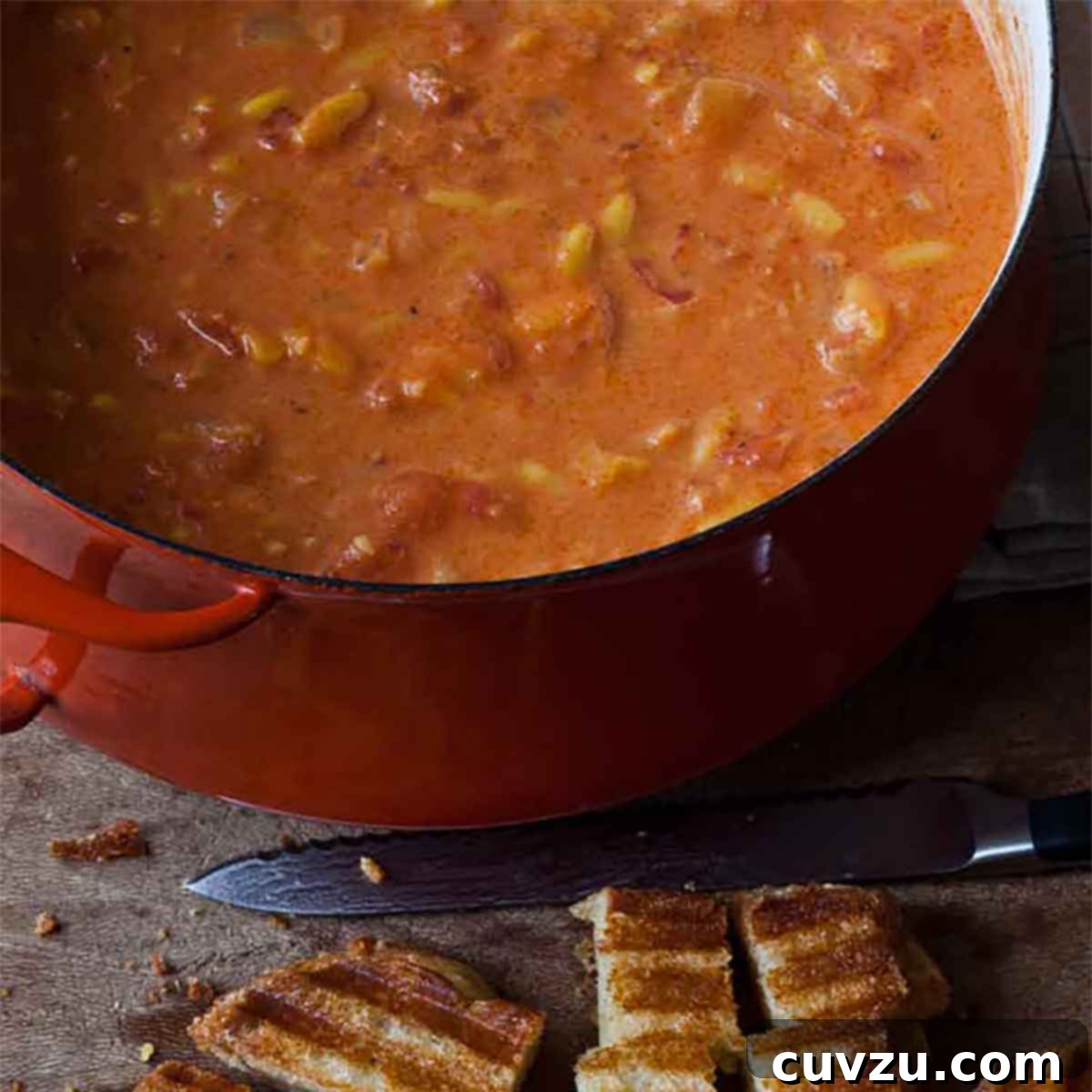 A large pot of Ina Garten's easy tomato soup with a grilled cheese sandwich being cut into croutons beside it, a comforting meal idea.