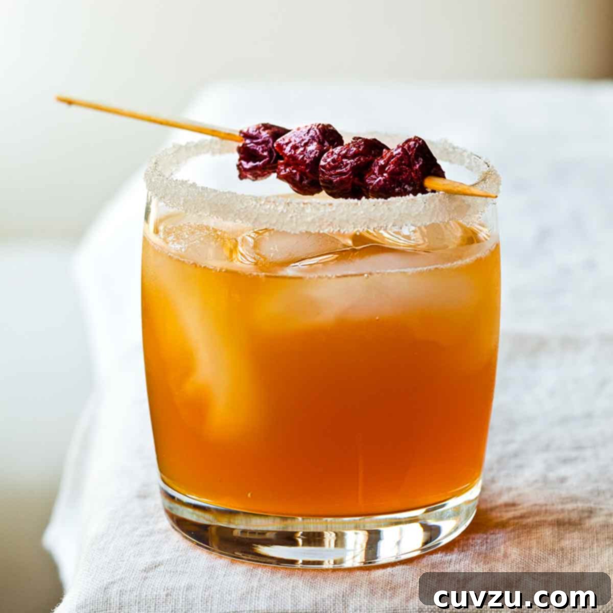 A sidecar cocktail, ice cubes and a dried cherry garnish, in a highball glass with a sugared rim, a classic Barefoot Contessa cocktail.