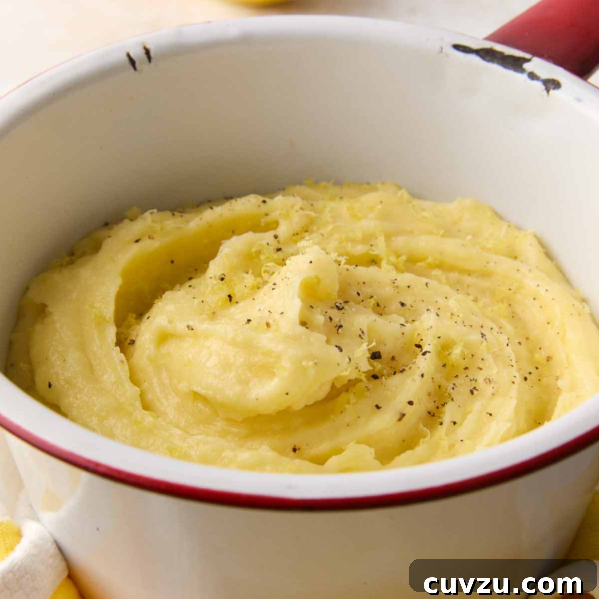 An enamel bowl filled with mashed potatoes, topped with black pepper and lemon zest, a signature Ina Garten side dish.
