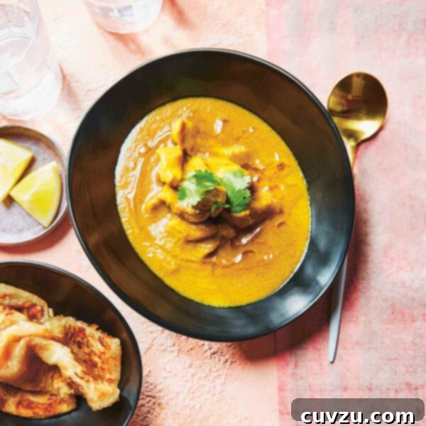 A black bowl filled with Macanese Portuguese chicken curry with dishes of naan and lemon wedges beside it.
