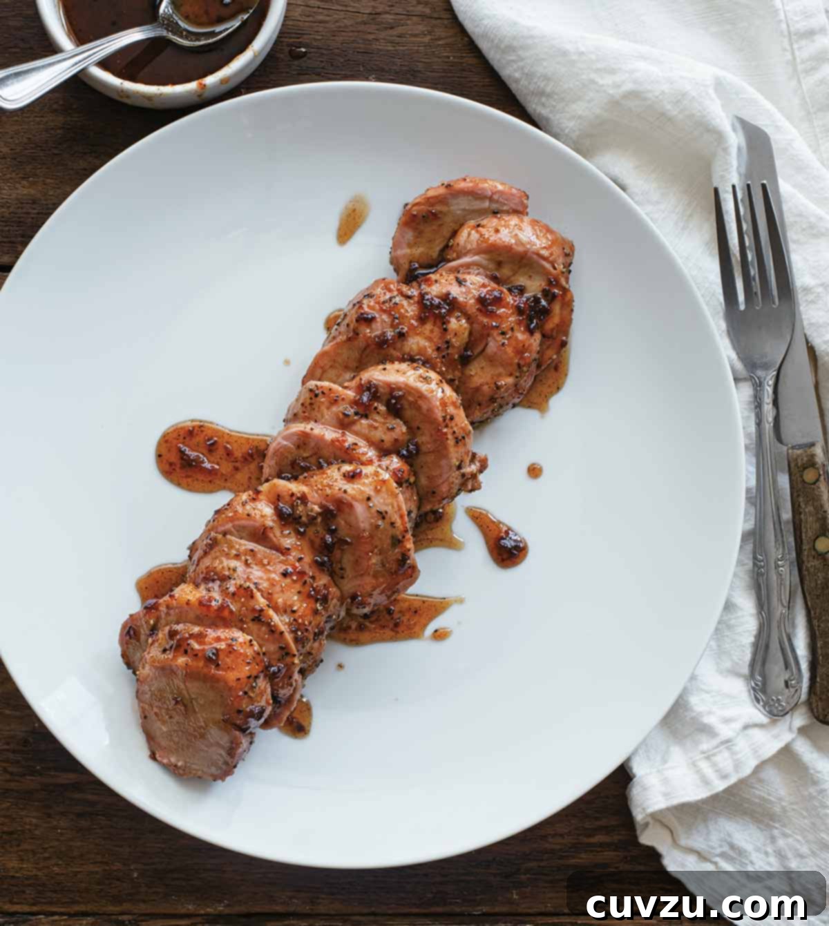 Maple-Glazed Smoked Pork Tenderloin with Chipotle Kiss 2 A sliced smoked pork tenderloin with maple chipotle glaze on a white plate, garnished with fresh herbs.
