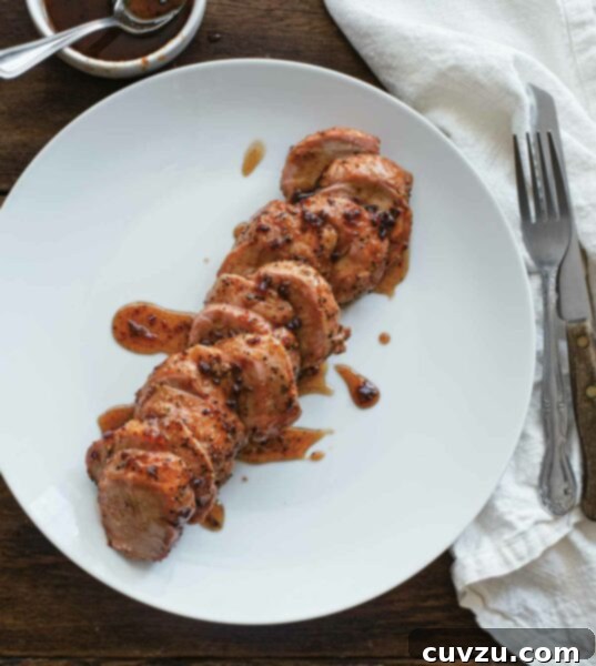 Maple-Glazed Smoked Pork Tenderloin with Chipotle Kiss 3 A sliced smoked pork tenderloin with maple chipotle glaze on a white plate.