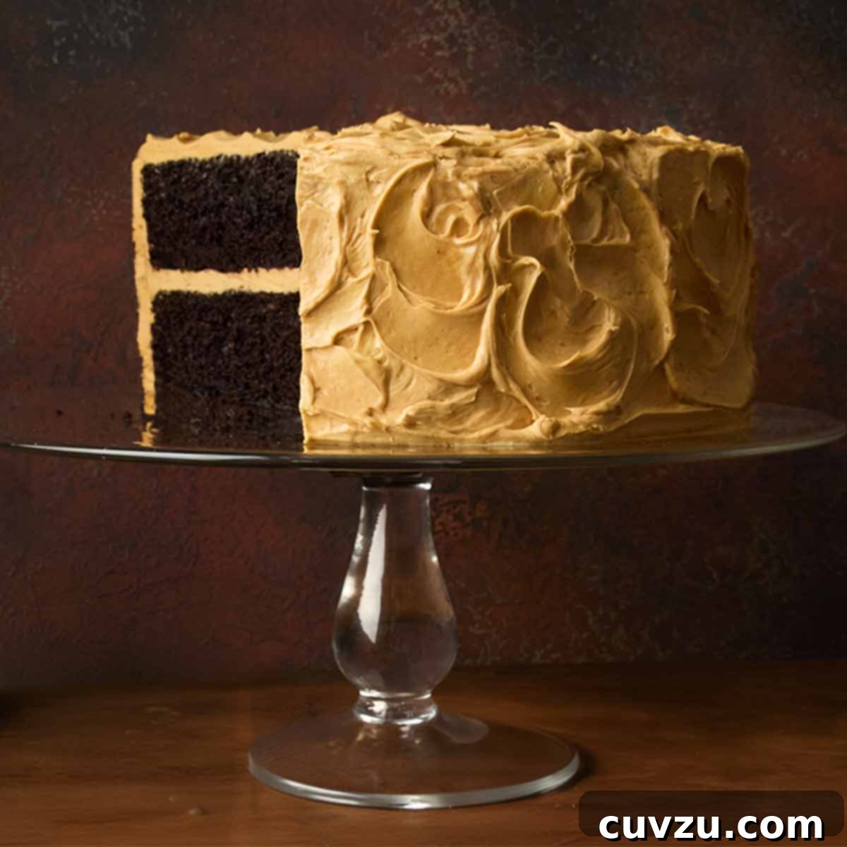 A chocolate caramel cake on a cake stand with a section cut from it.
