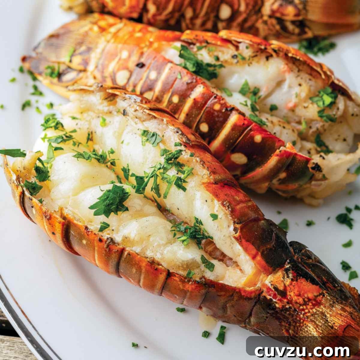 Three grilled lobster tails on an oval platter, garnished with chopped parsley.