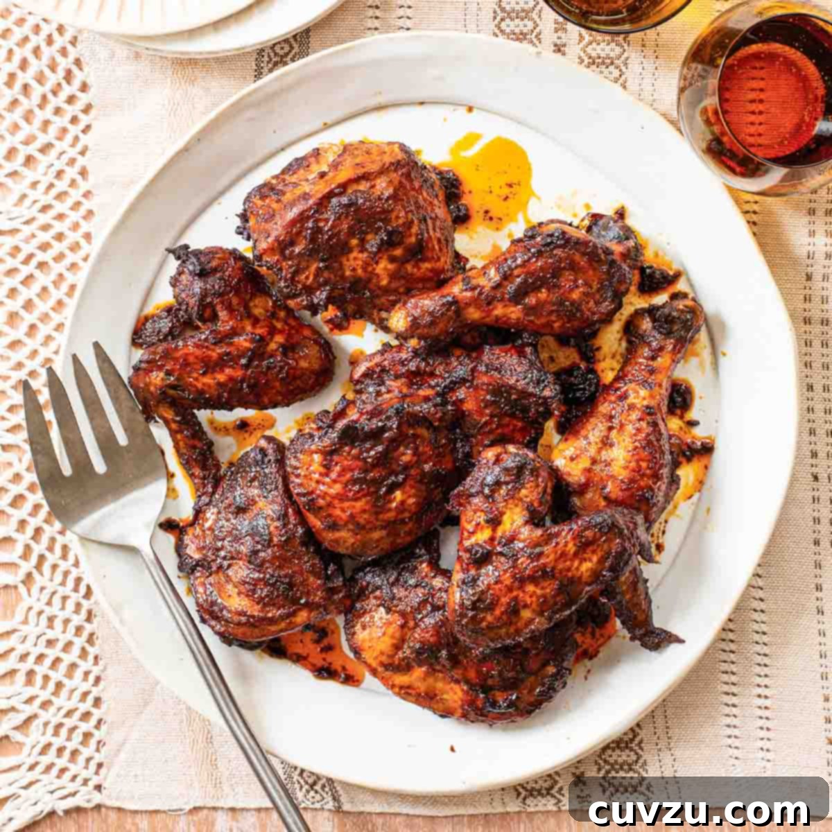 Garlic, chile, and cumin roast chicken on a white platter with a serving fork, beside empty plates and glasses of wine.