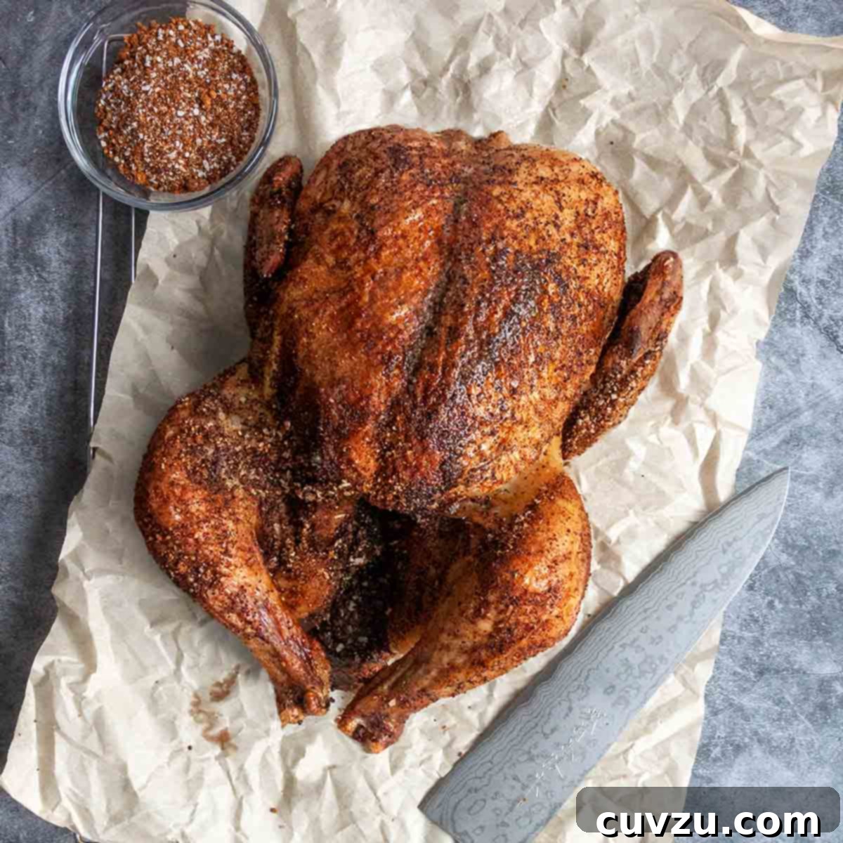 Elevate Your BBQ: 14 Must-Try Smoker Recipes 10 A smoked chicken on a piece of crumpled parchment paper with a knife and a bowl of spice rub on the side.