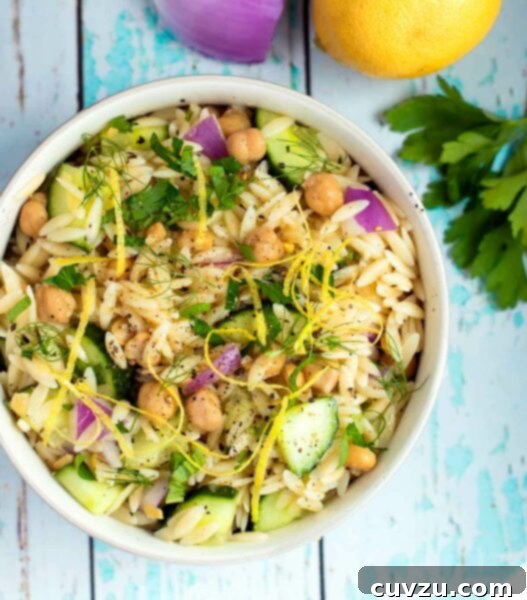 A white bowl filled with vegan chickpea and orzo salad with lemon zest garnish.