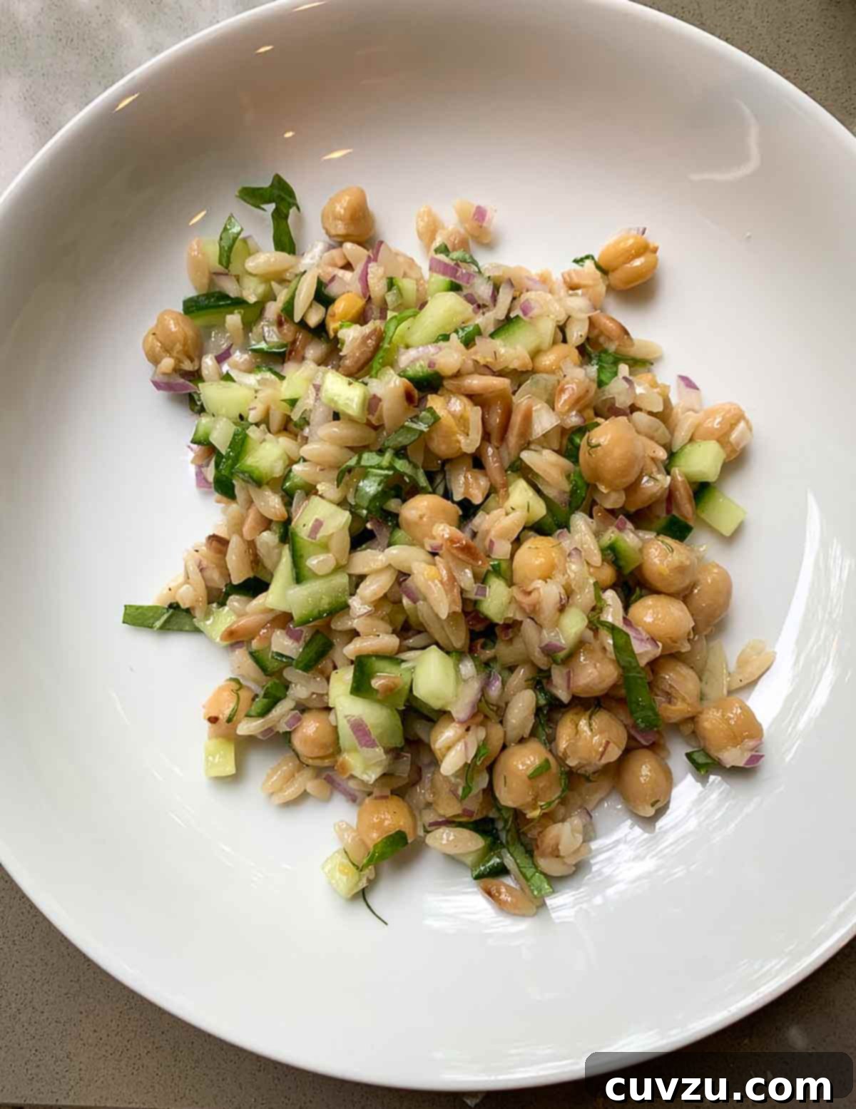 Zesty Vegan Chickpea Orzo Medley 5 A white bowl filled with vegan chickpea and orzo salad with lemon zest garnish.