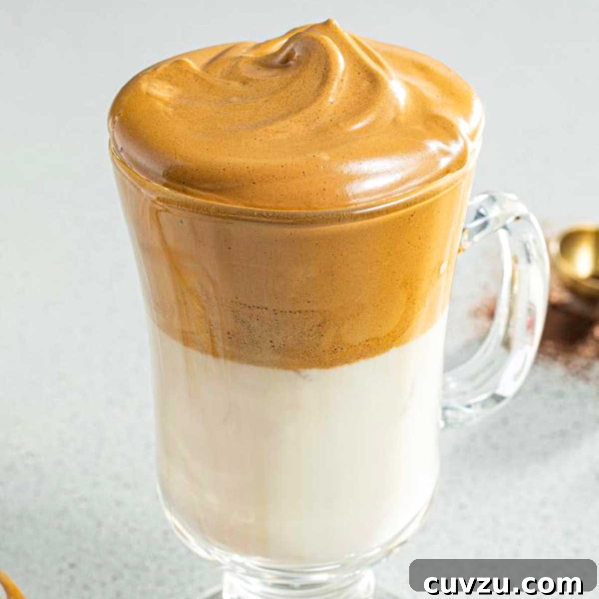 Cloud Coffee 2 A tall glass filled with creamy, light brown whipped coffee foam sitting atop a layer of cold milk with ice cubes, garnished with a sprinkle of coffee powder.