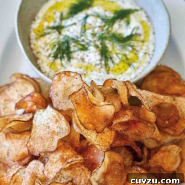 A white oval platter holding a bowl of dill dip with potato chips beside it.