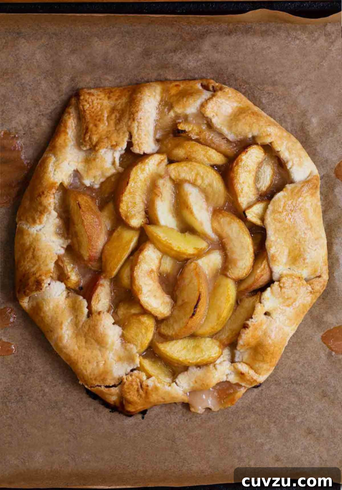 A white peach crostata--slices of white peaches in a circle of dough folded over on the edges sitting a sheet of parchment.