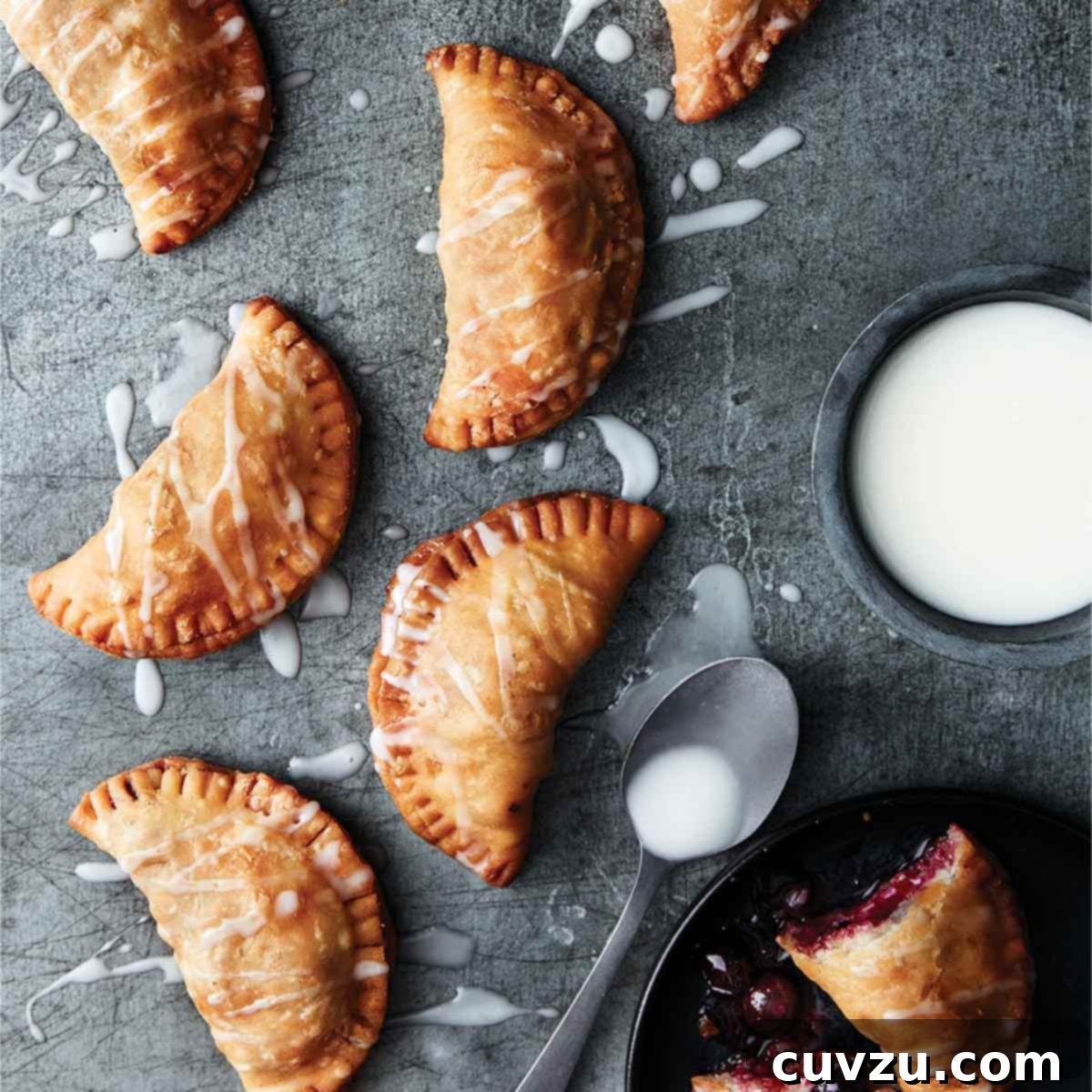 8 crescent-shape blueberry fried pies with Meyer lemon drizzle sauce nearby all on a piece of slate