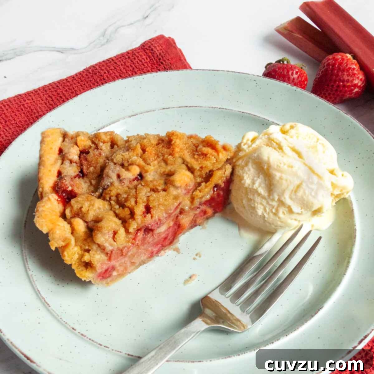 A slice of strawberry rhubarb pie on a green plate with a scoop of ice cream and a fork on the side.