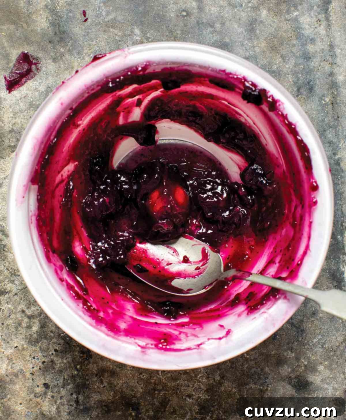 A white bowl with a little bit of stovetop fruit pie filling in the bottom and a spoon resting inside.